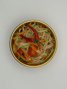 Papaya salad with carrots, tomatoes, and chilies in a gold bowl